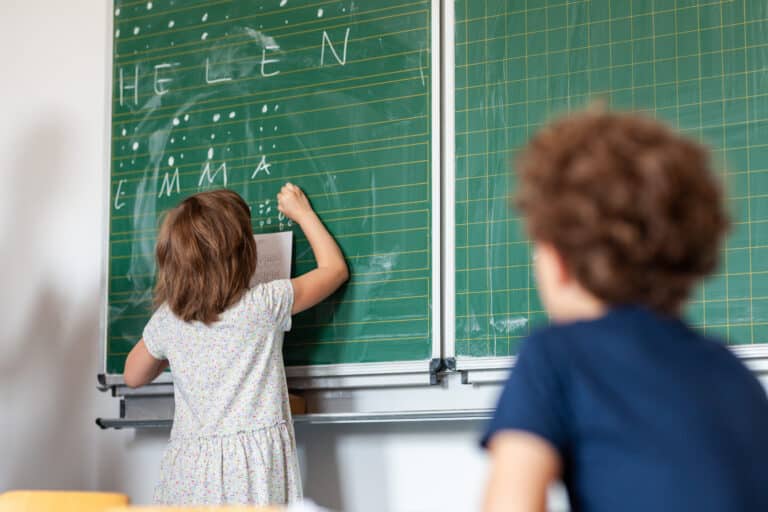 Kinder schreiben Namen an eine grüne Tafel
