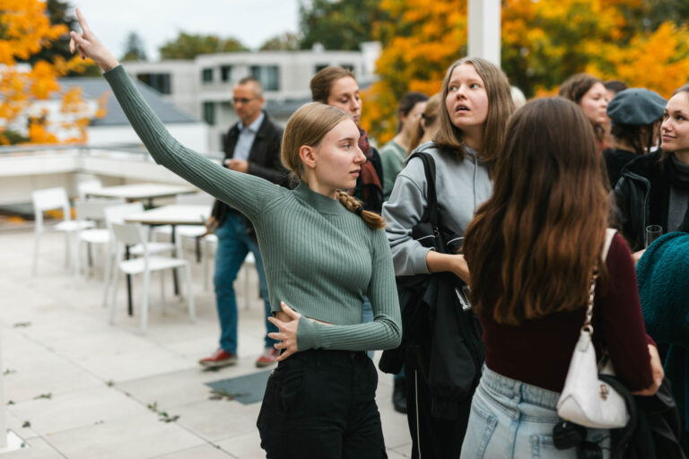 Studentin winkt in einer Gruppe auf der Dachterrasse